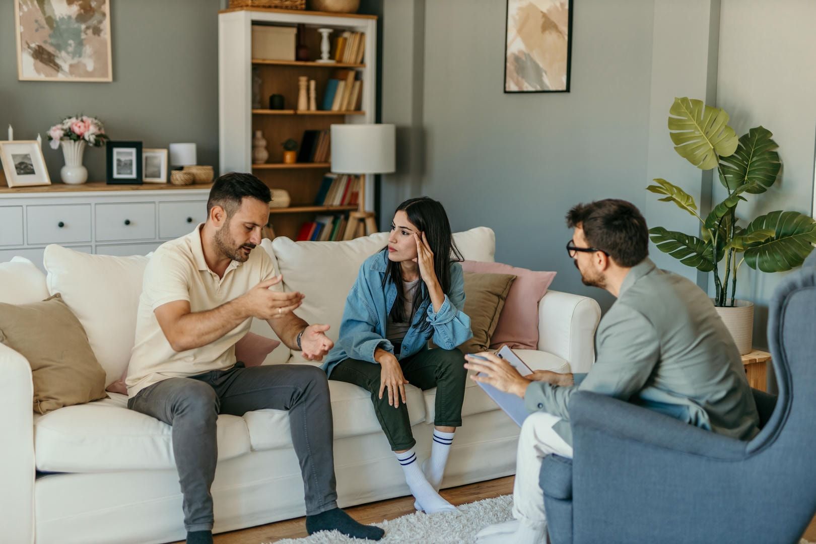 A group of people are sitting on a couch talking to each other in a living room.