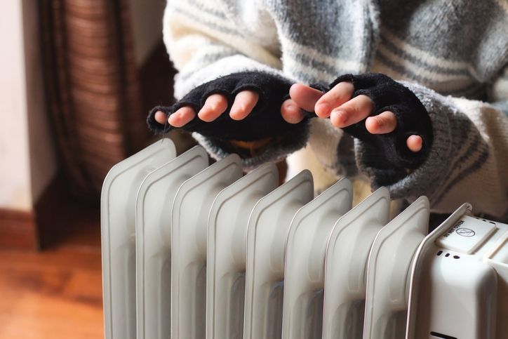 Person heating their hands at home over a domestic portable radiator in winter.