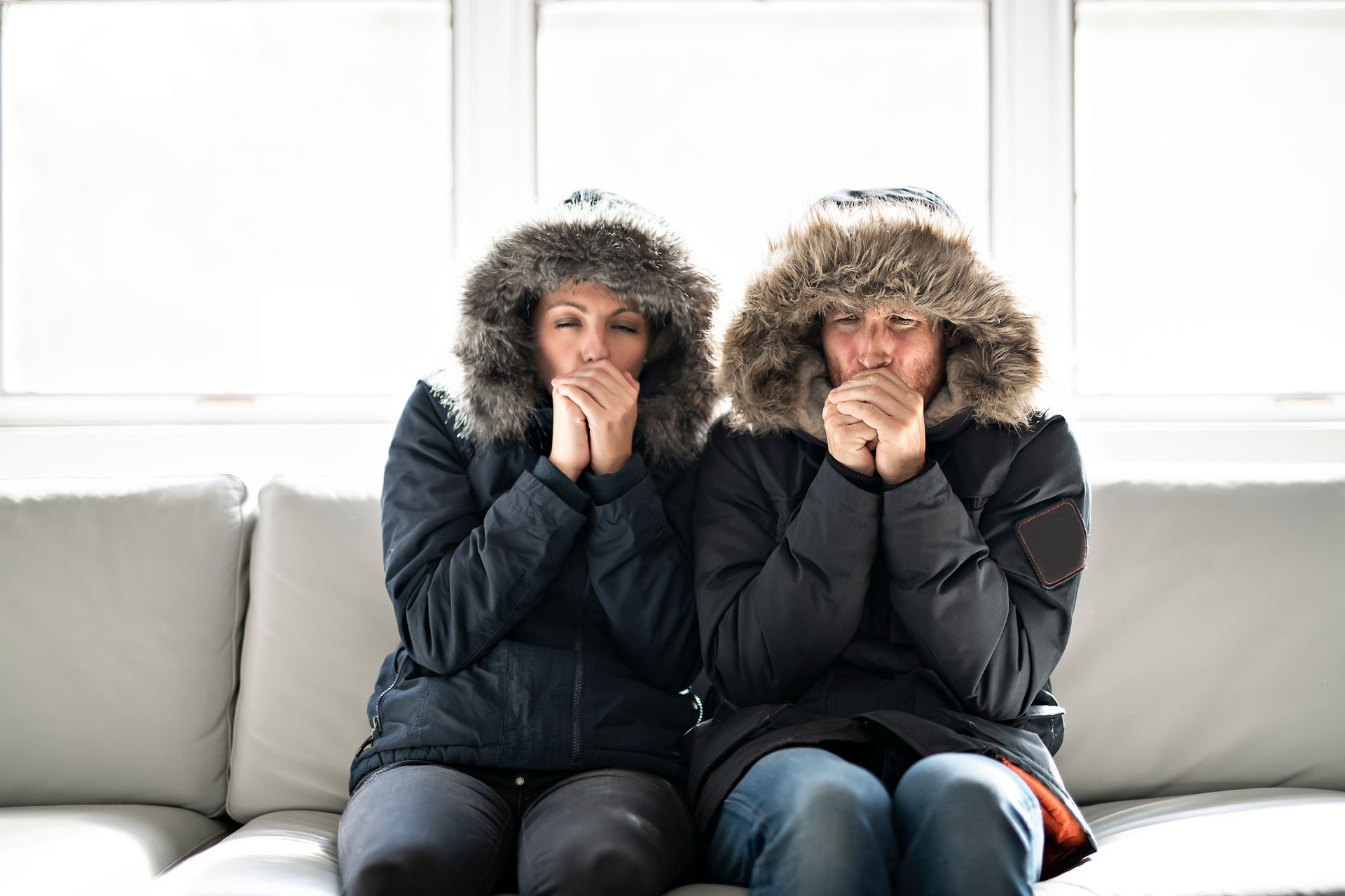 A couple wearing coats on the couch representing common heating problems in a Tennessee home.