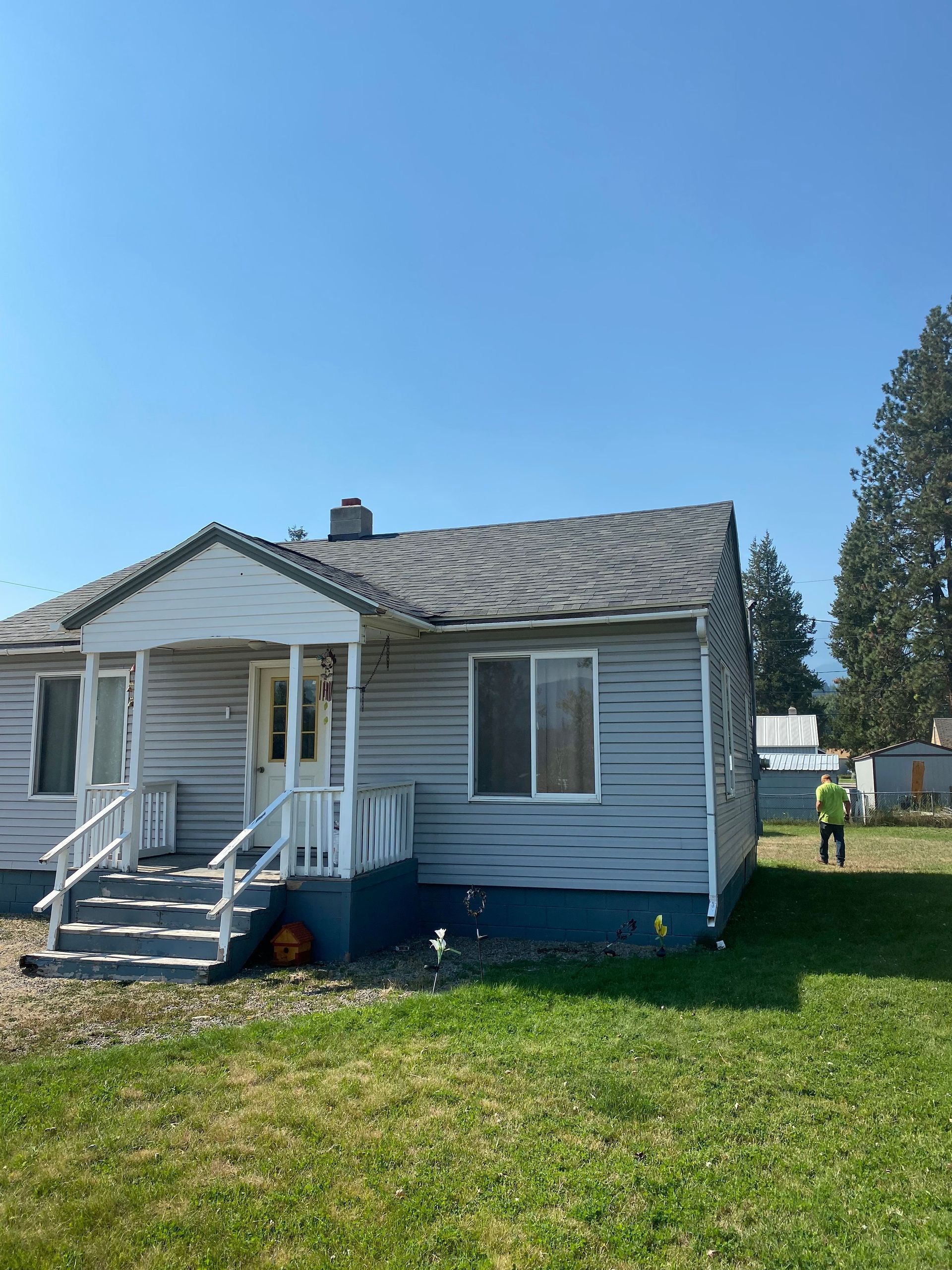 A small white house with a gray roof is sitting in the middle of a lush green field.