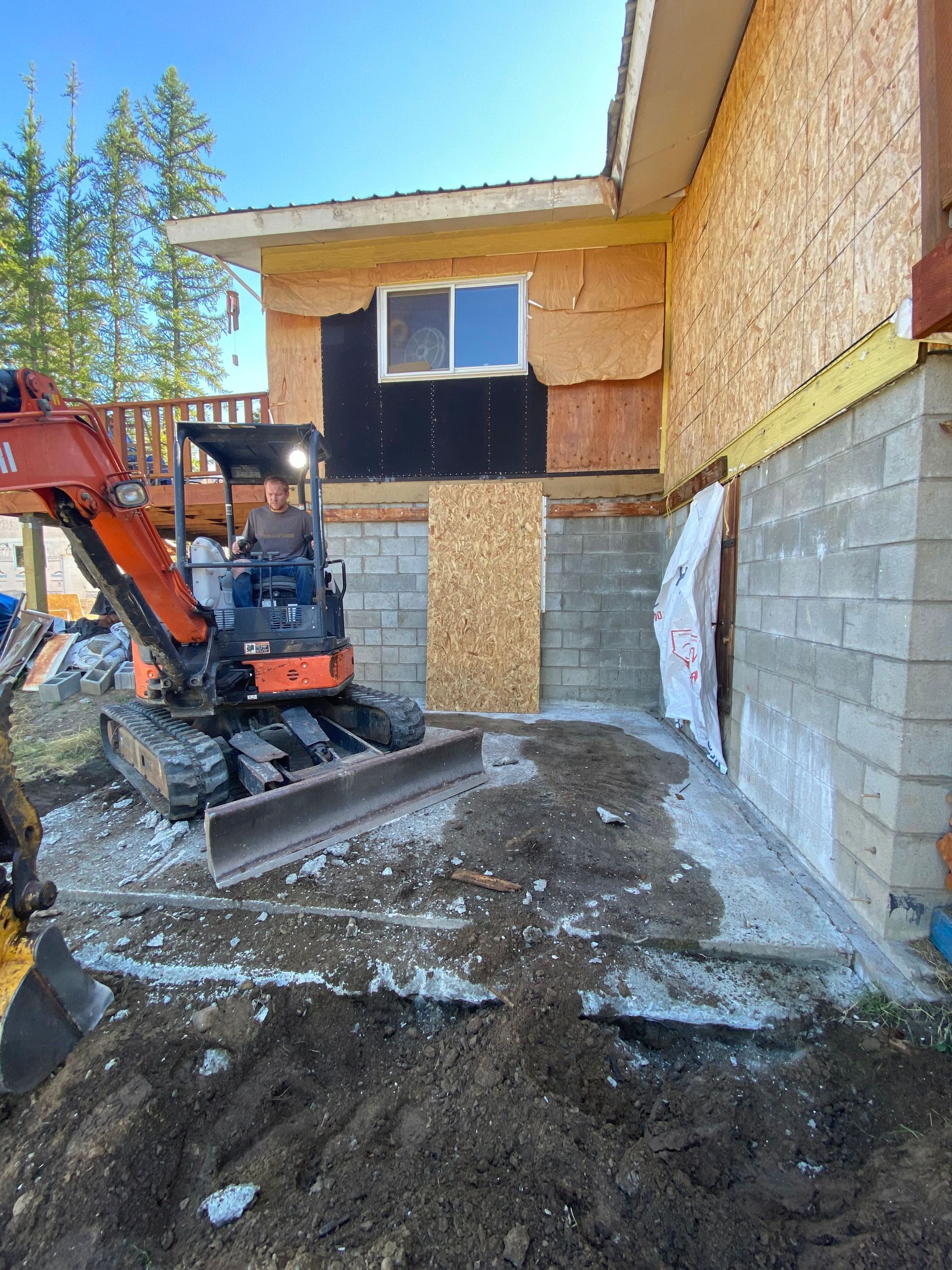 A man is driving an excavator in front of a house under construction.