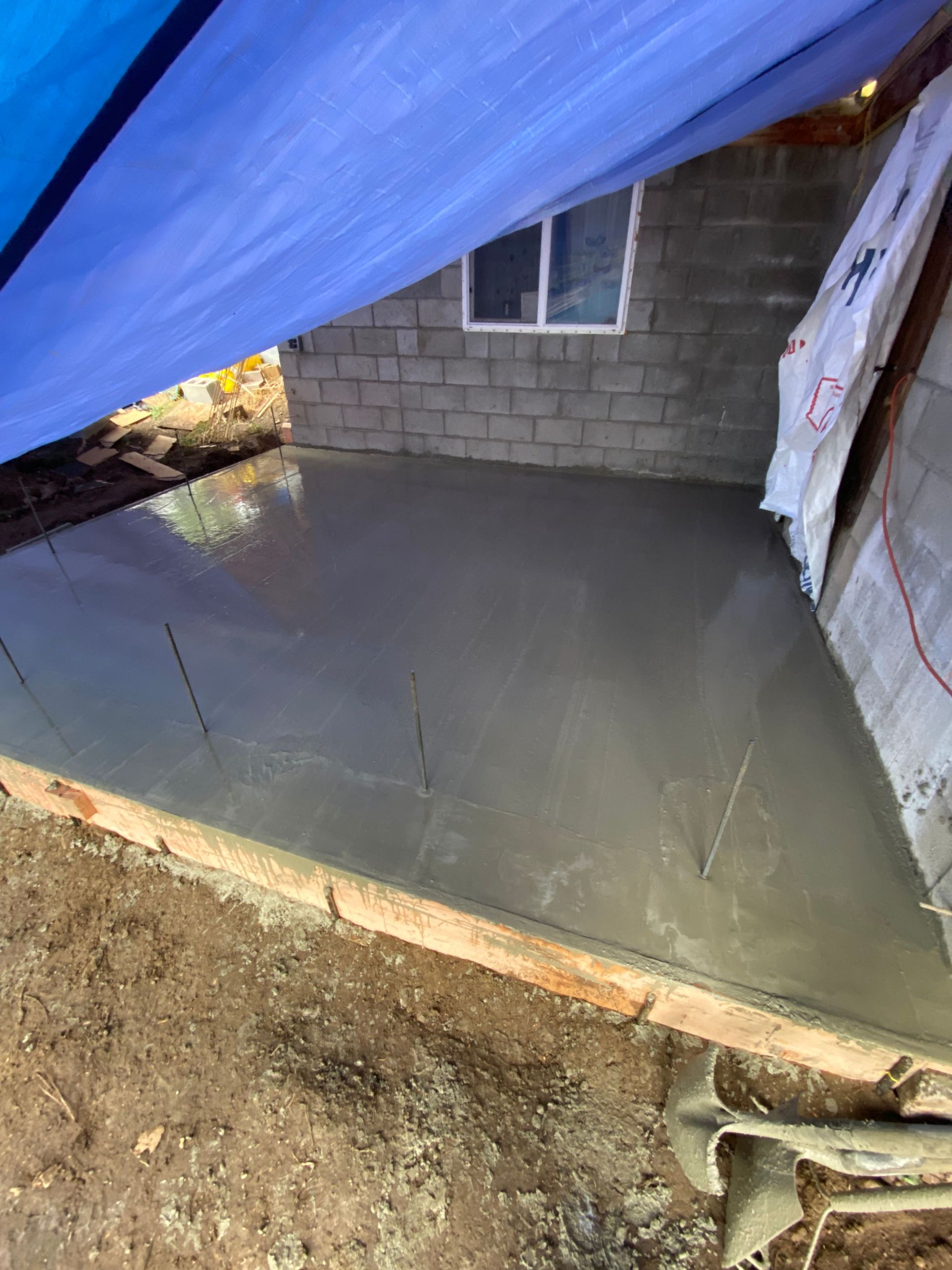 A blue tarp is covering a concrete floor in front of a brick building.