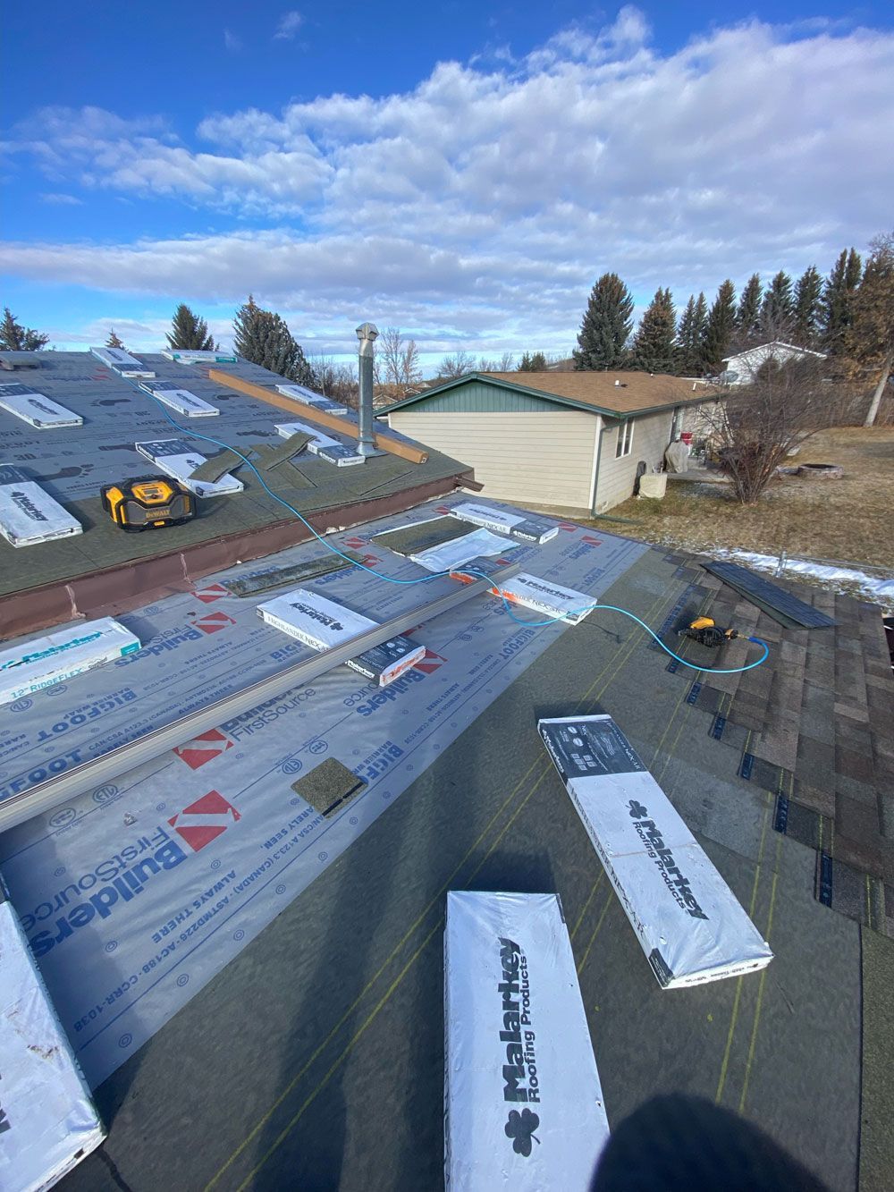 A roof with a lot of shingles on it and a house in the background.