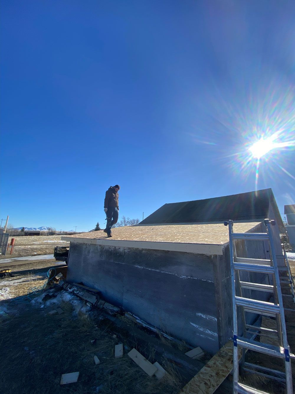 A man is standing on top of a roof next to a ladder.