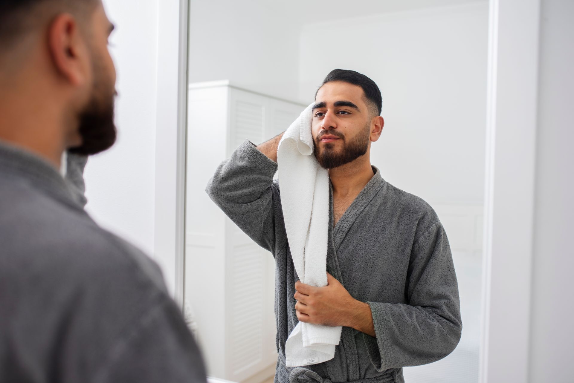 A man is wiping his face with a towel in front of an anti-fog mirror.