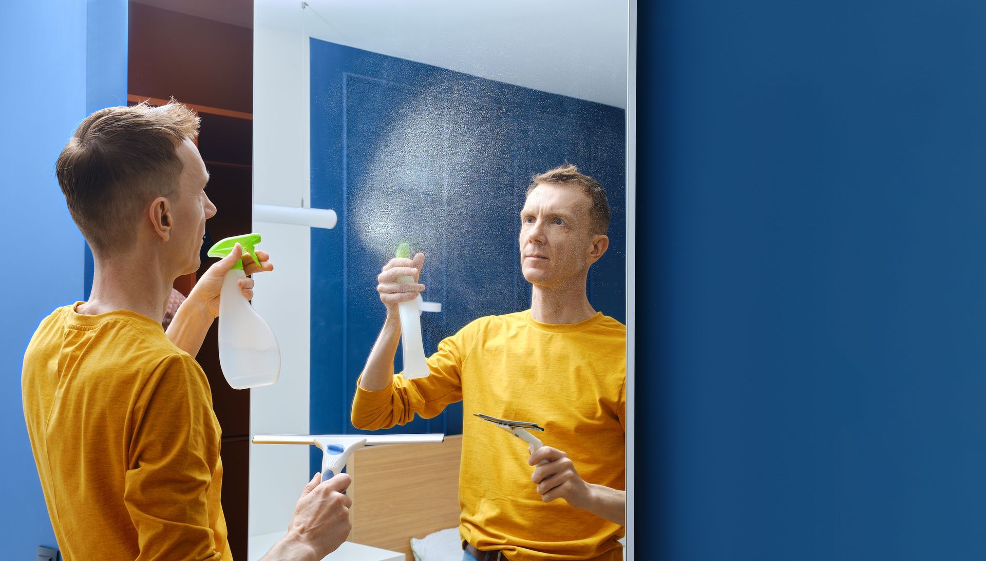 A man is cleaning a bathroom mirror with a spray bottle.