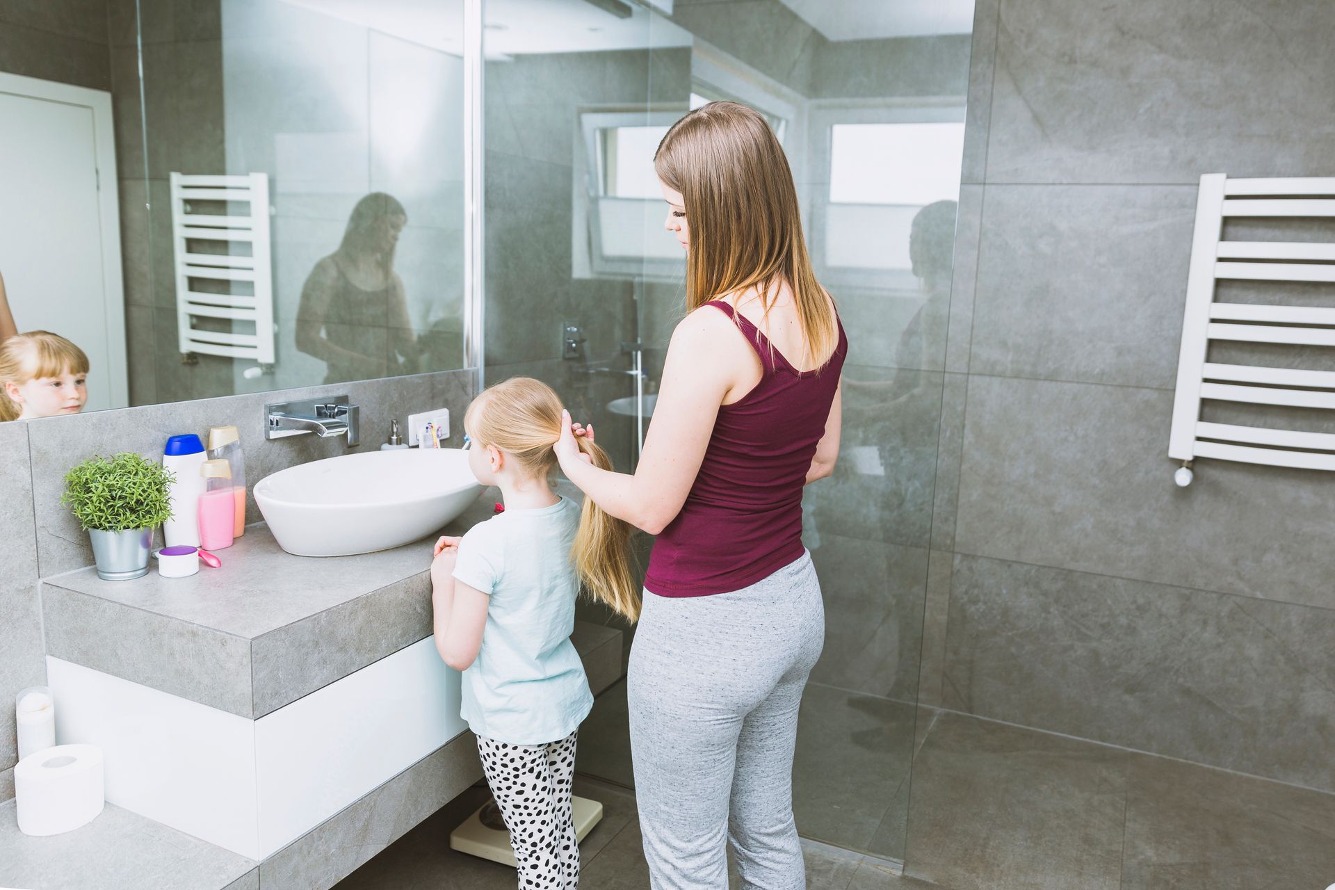 A woman is brushing a little girl 's hair in a bathroom.