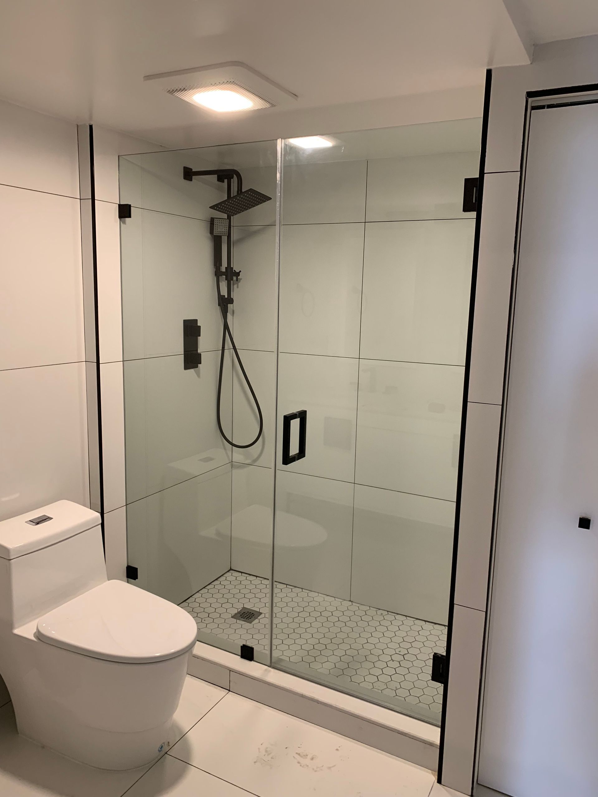 A bathroom with a toilet , shower , and glass shower door.