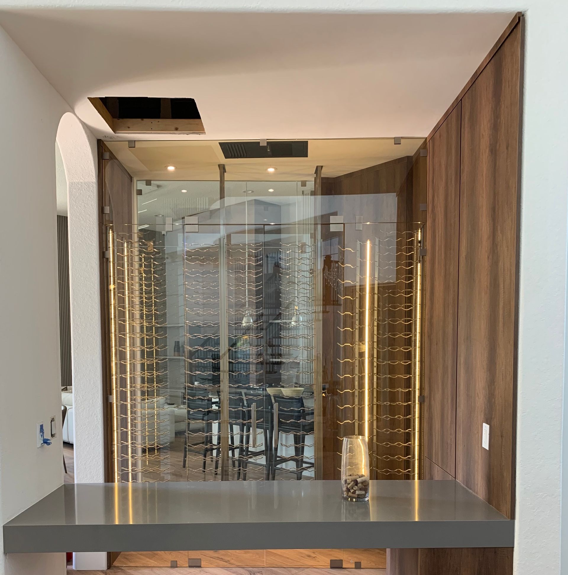 There is a table in the middle of a room with a wine cellar in the background.