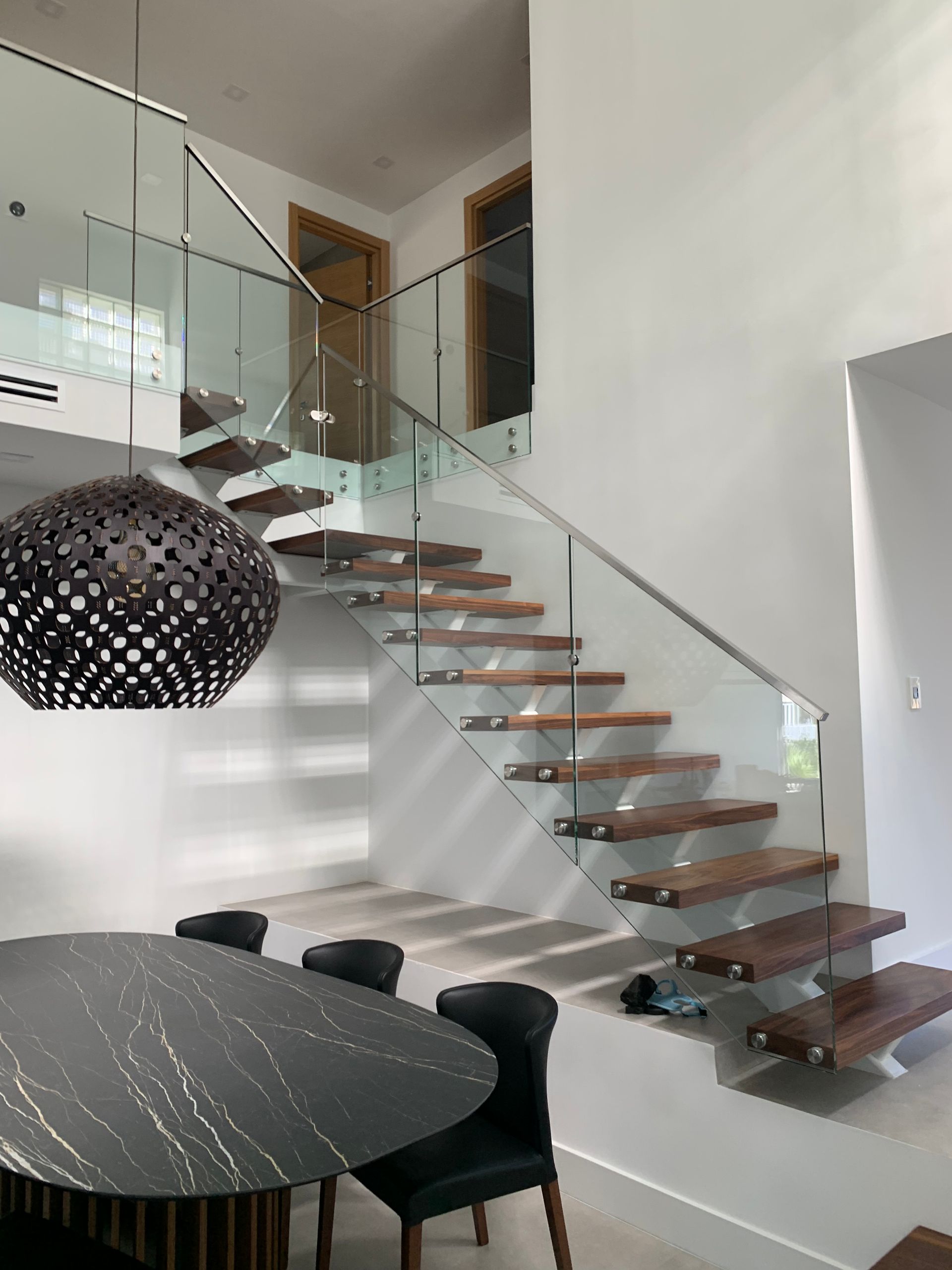 A dining room with a table and chairs and a staircase with a glass railing.