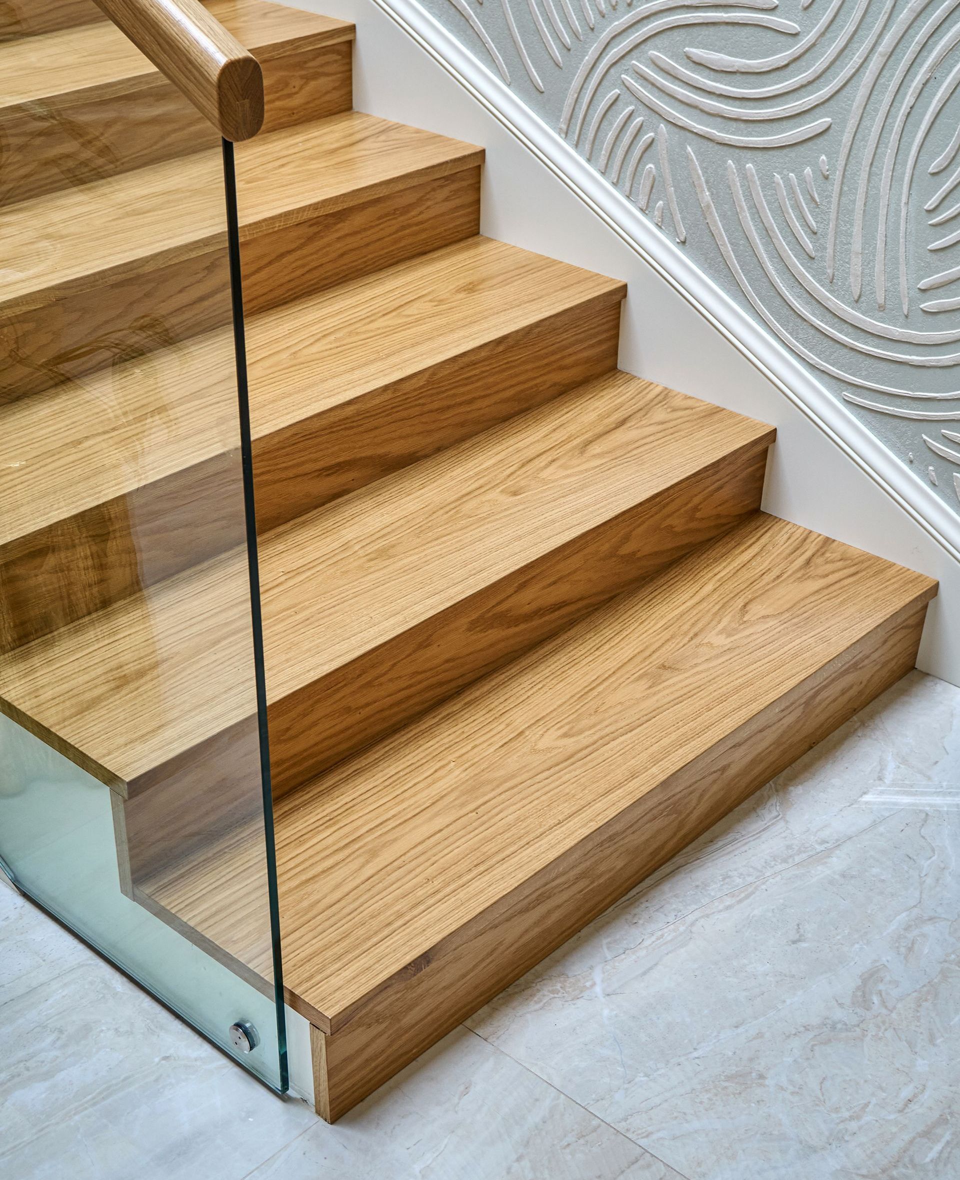 A close up of a wooden staircase with a glass railing.