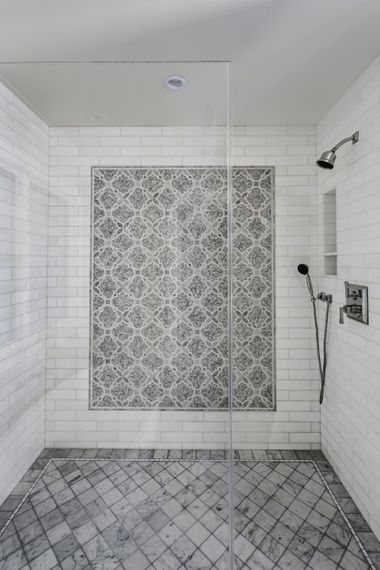 A bathroom with white tiles and a walk in shower with a glass door.