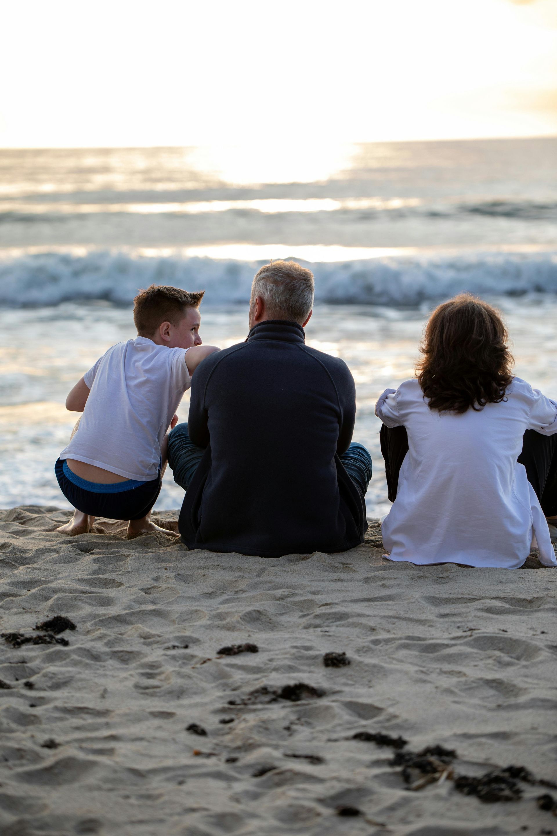 A family is sitting on the beach looking at the ocean.