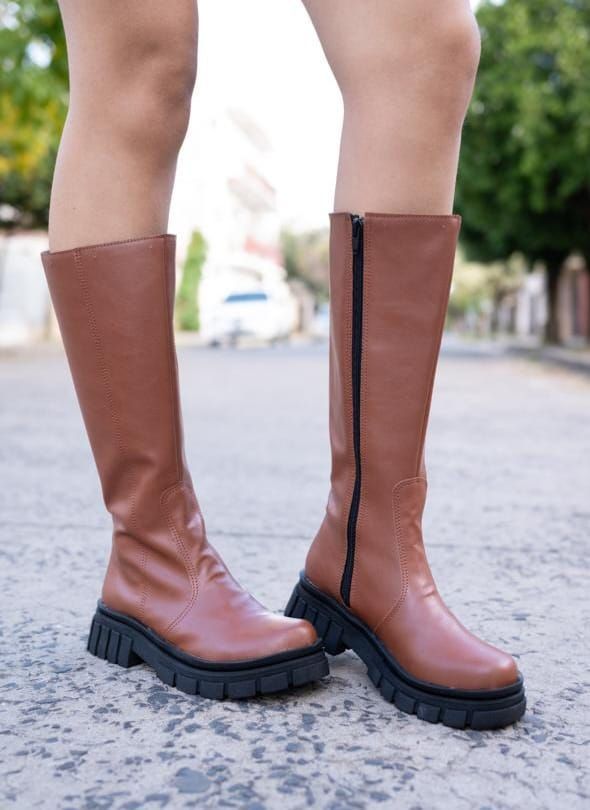 Botas hasta la rodilla de piel marrón con suela negra y cremallera, para exterior en la calle.