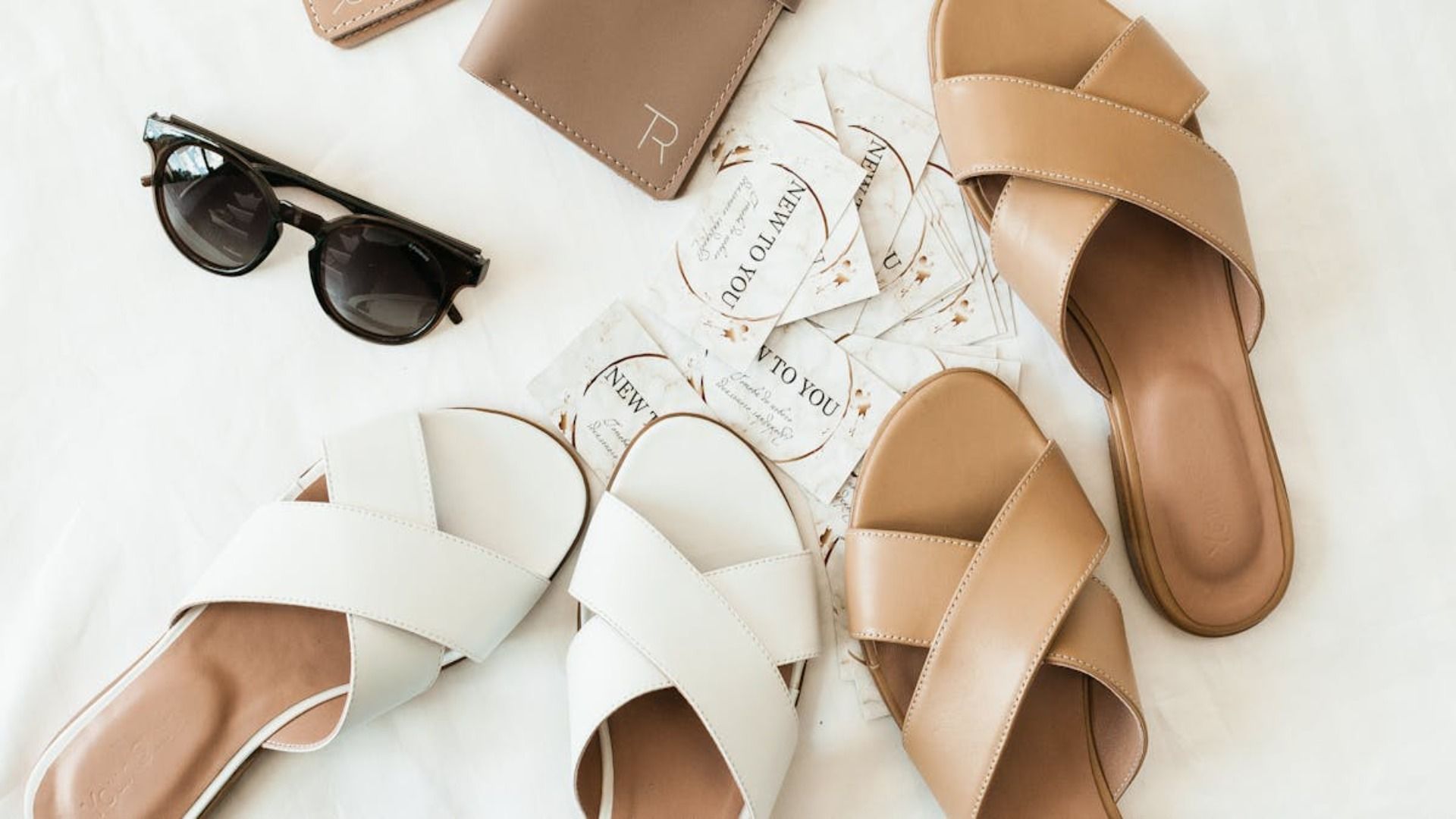 Un par de sandalias, gafas de sol, un pasaporte y una billetera están sobre una cama.