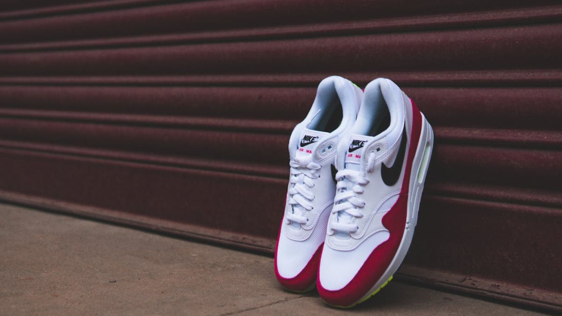 Un par de zapatillas Nike Air Max blancas y rojas están apoyadas contra una pared.