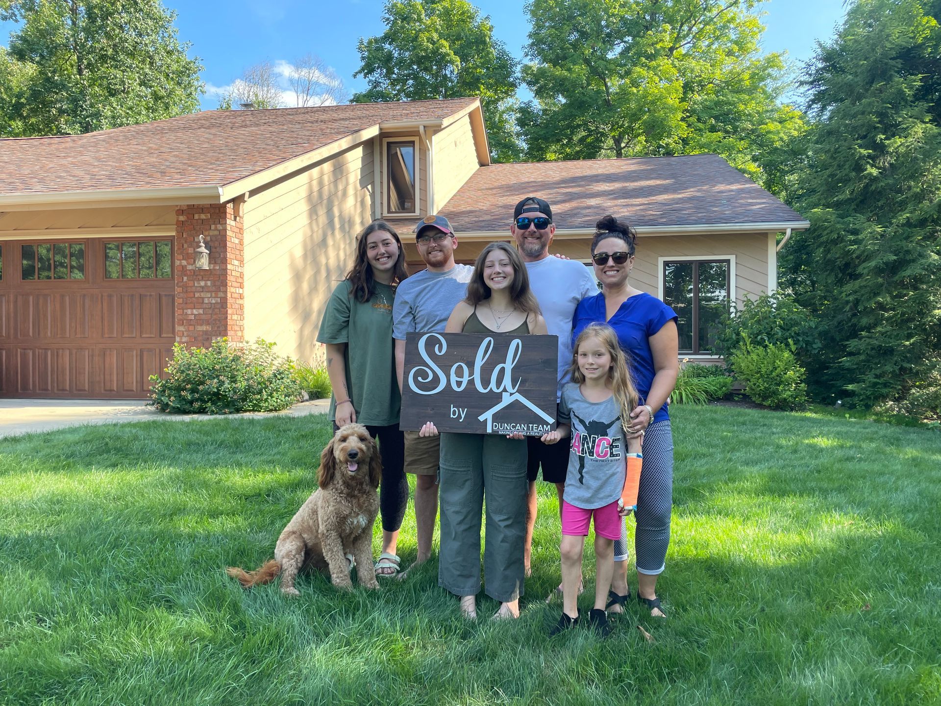 A family is standing in front of a house holding a sold sign.