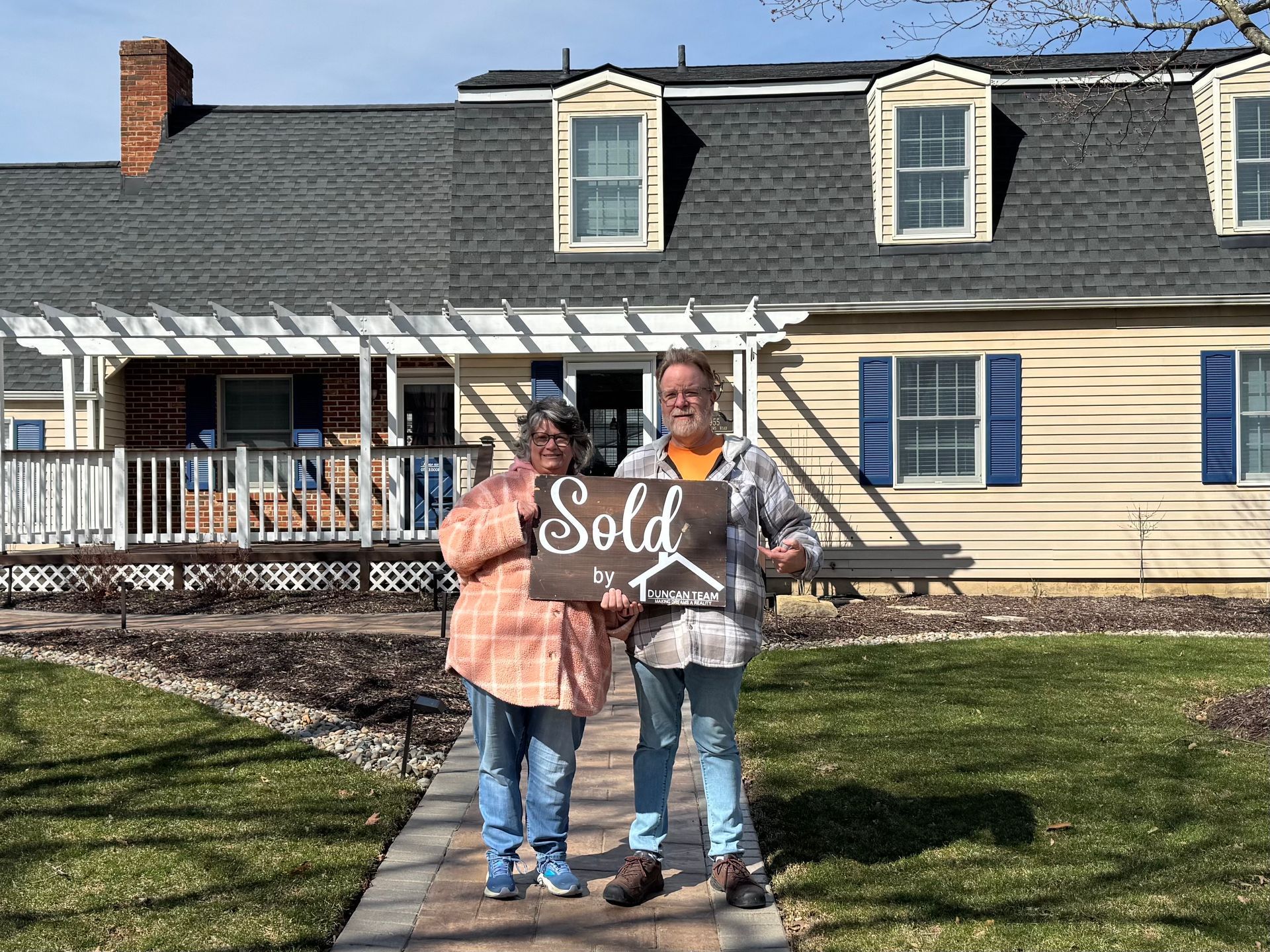 A family is standing in front of a house holding a sold sign.