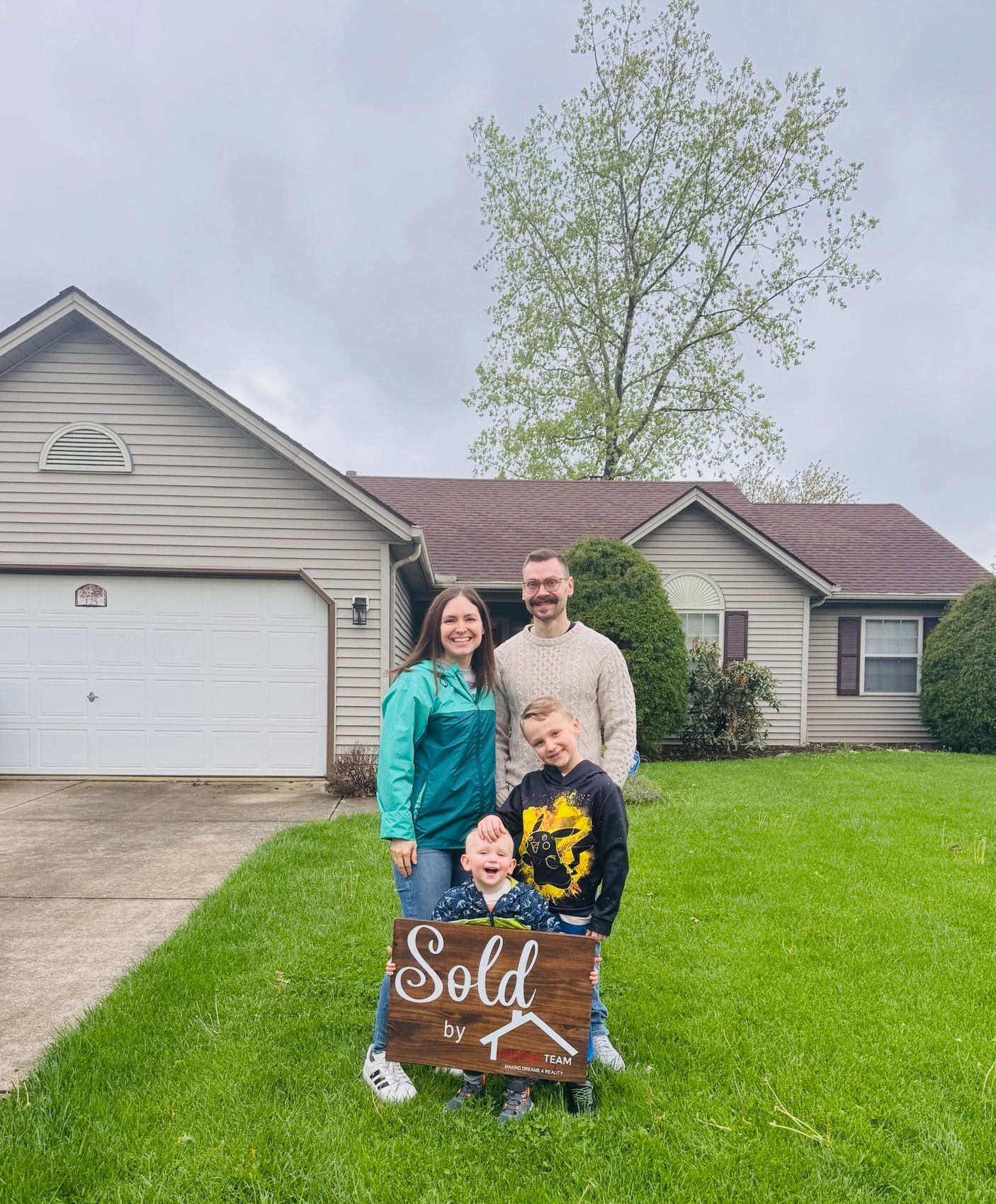 A family is standing in front of a house holding a sold sign.