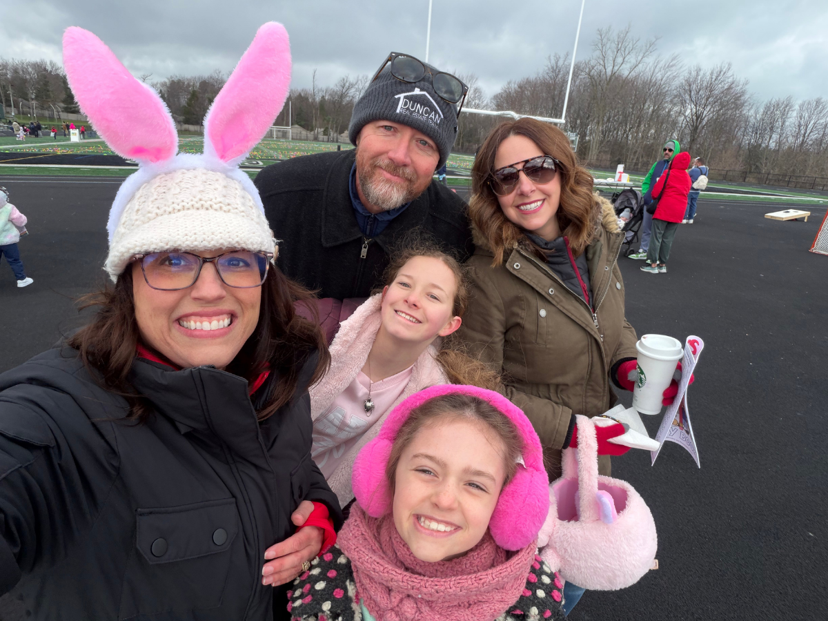 A family is standing in front of a house holding a sold sign.