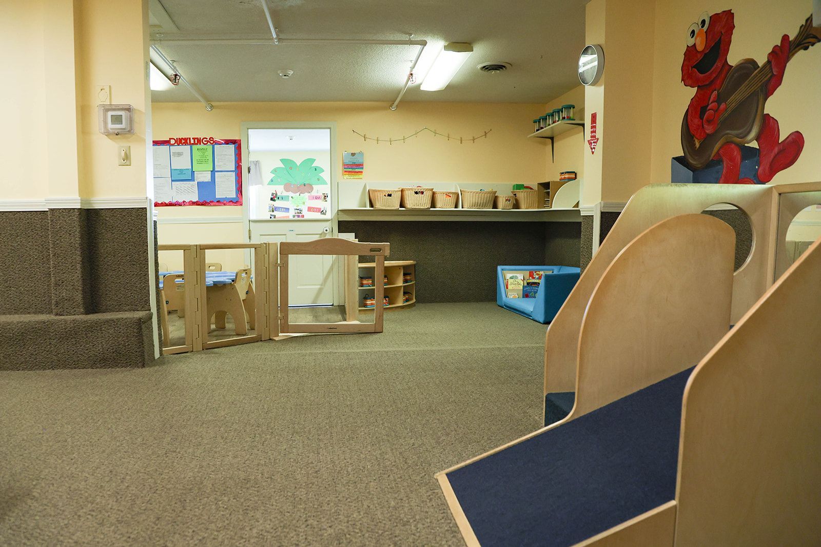 Playroom with Elmo art, wooden play structures, and a low fence.