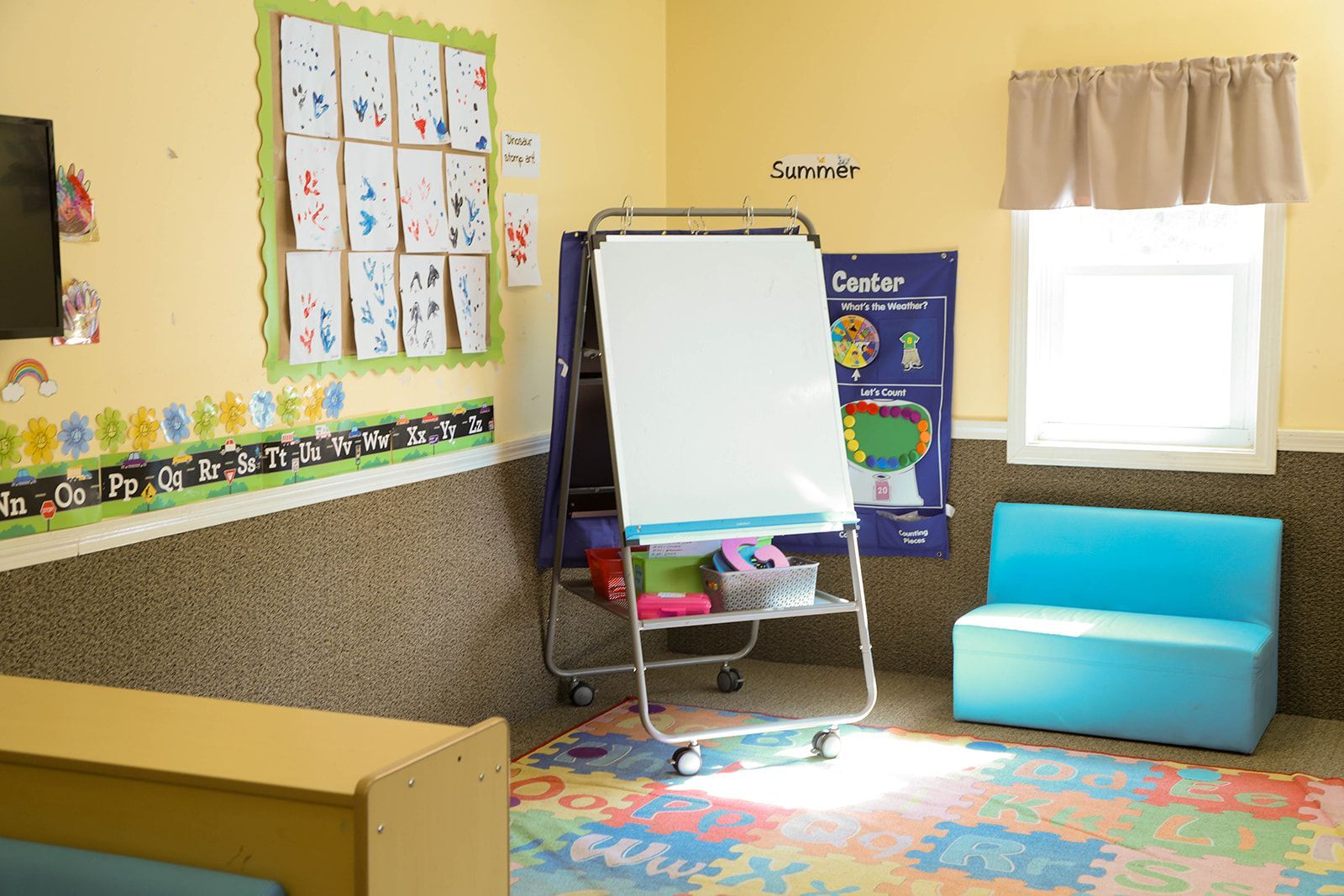 Classroom interior with whiteboard, artwork, colorful rug, and blue bench.
