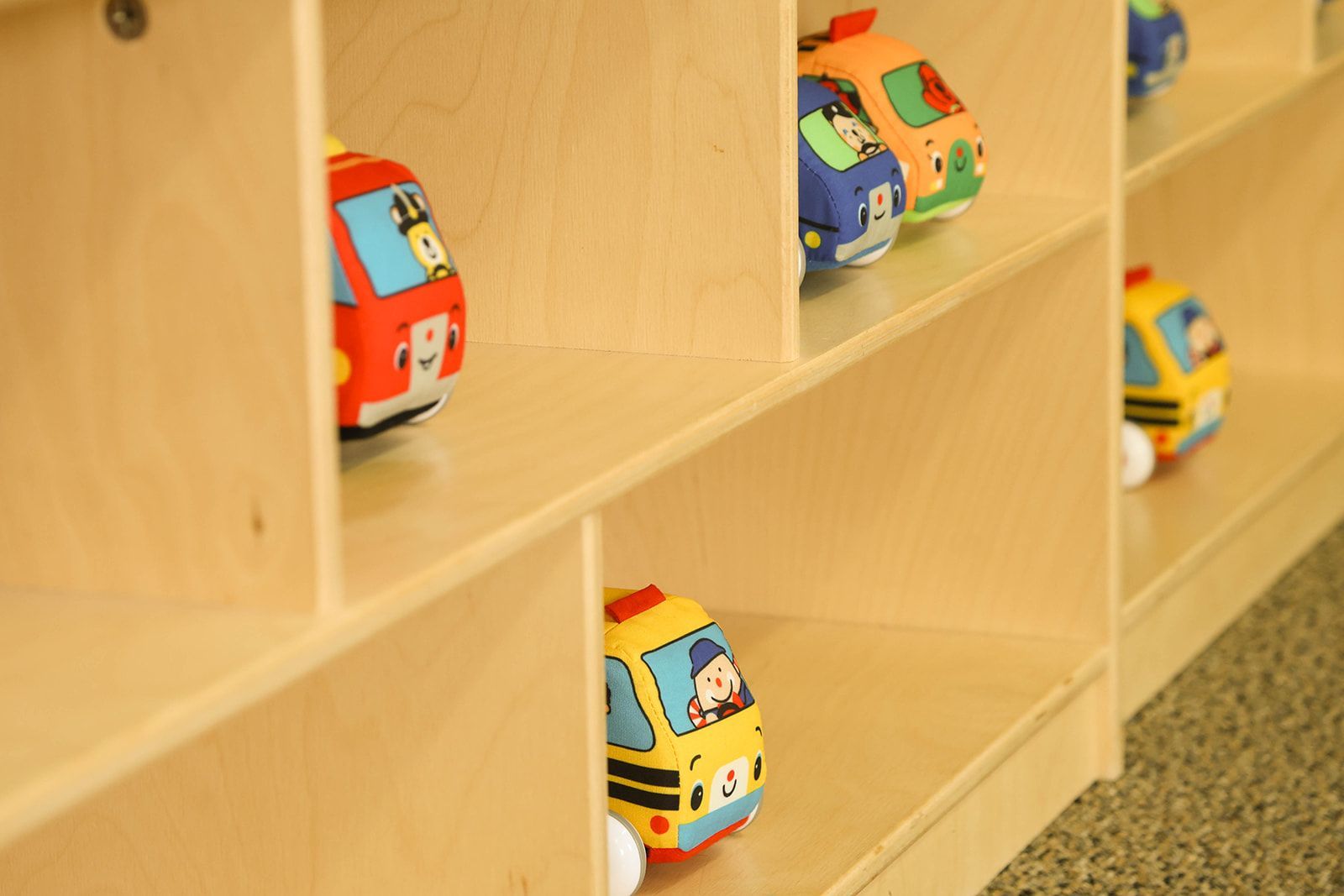 Colorful toy buses in wooden cubby shelves.