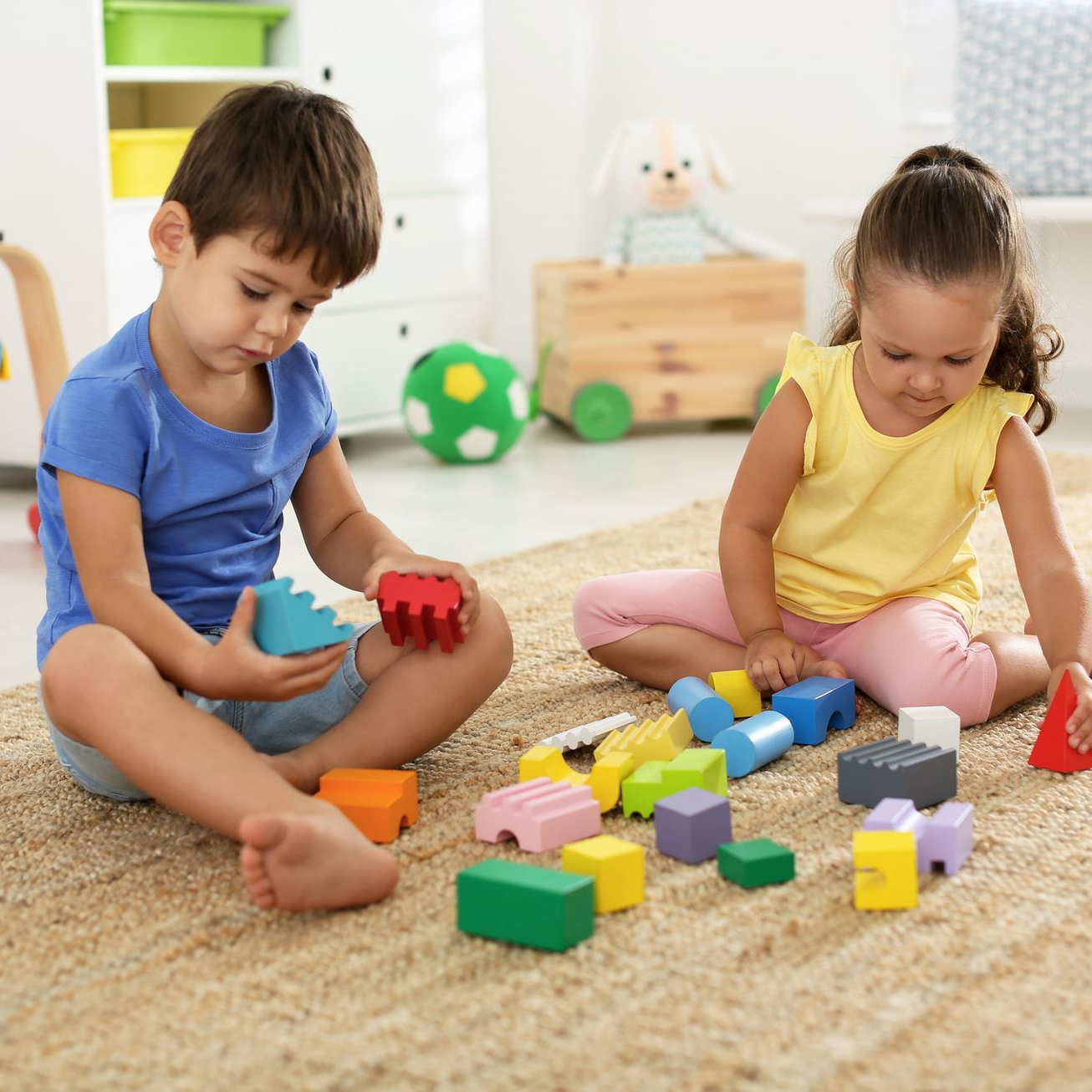 Two children playing with colorful wooden blocks on a carpeted floor.