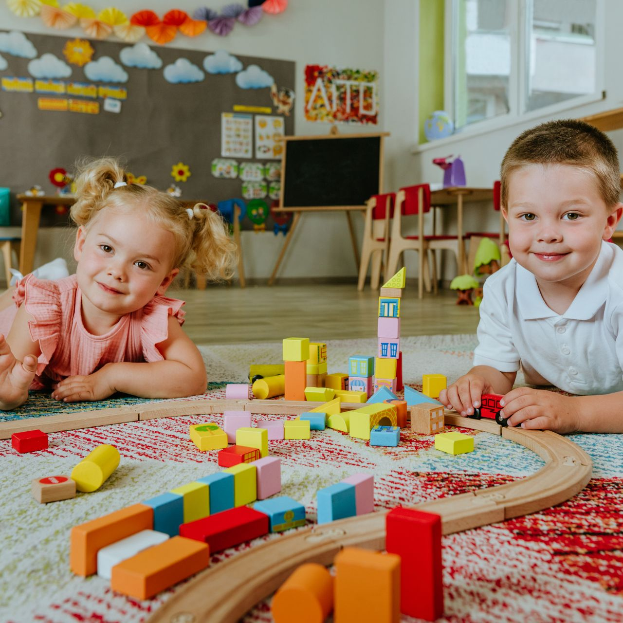 Two children playing with blocks and a toy train in a brightly decorated playroom.