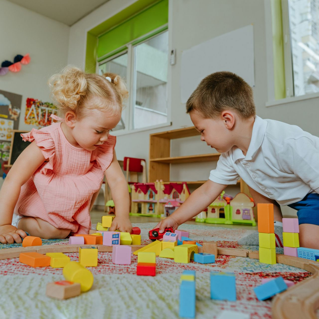 Two children playing with colorful wooden blocks on a rug in a playroom.