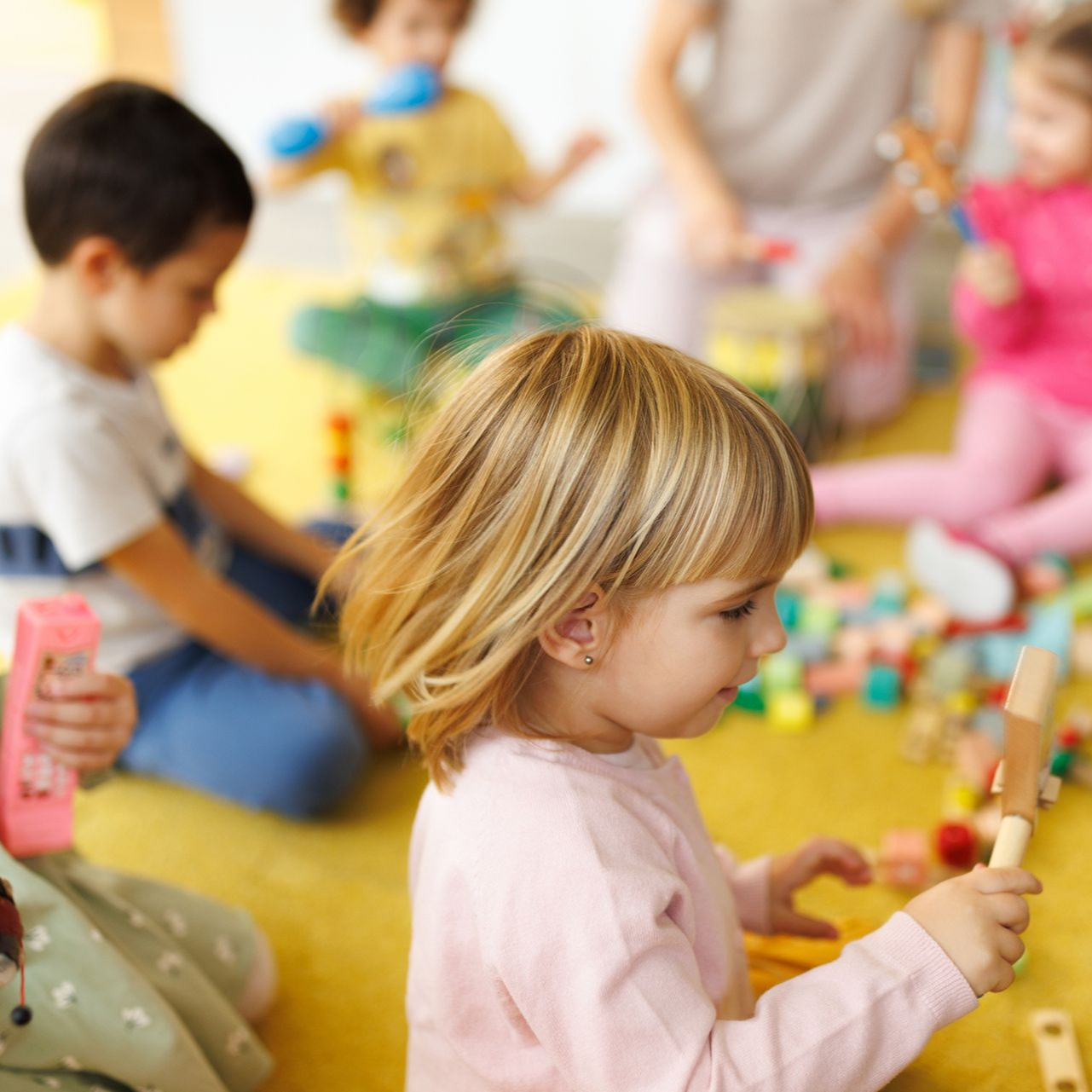 Children playing with blocks and toys on a yellow floor at a childcare center.