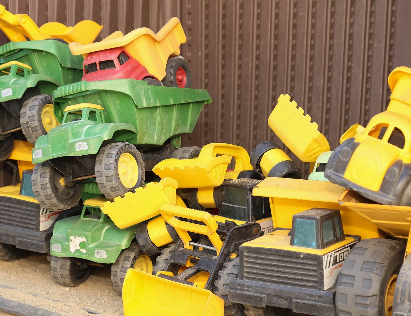 Pile of colorful toy dump trucks and bulldozers; green, yellow, and red.
