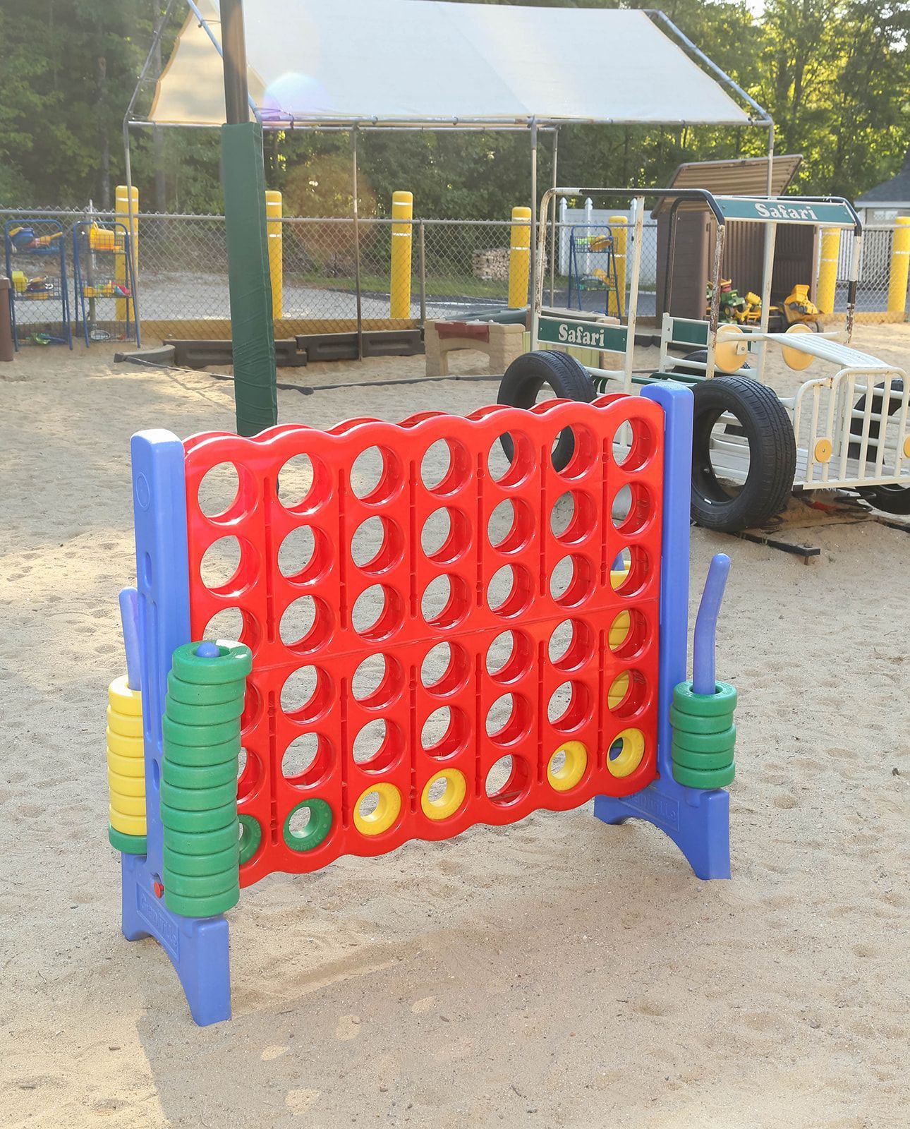Playground with spring horse and tractor toys, tan shade sails, and trees in the background.