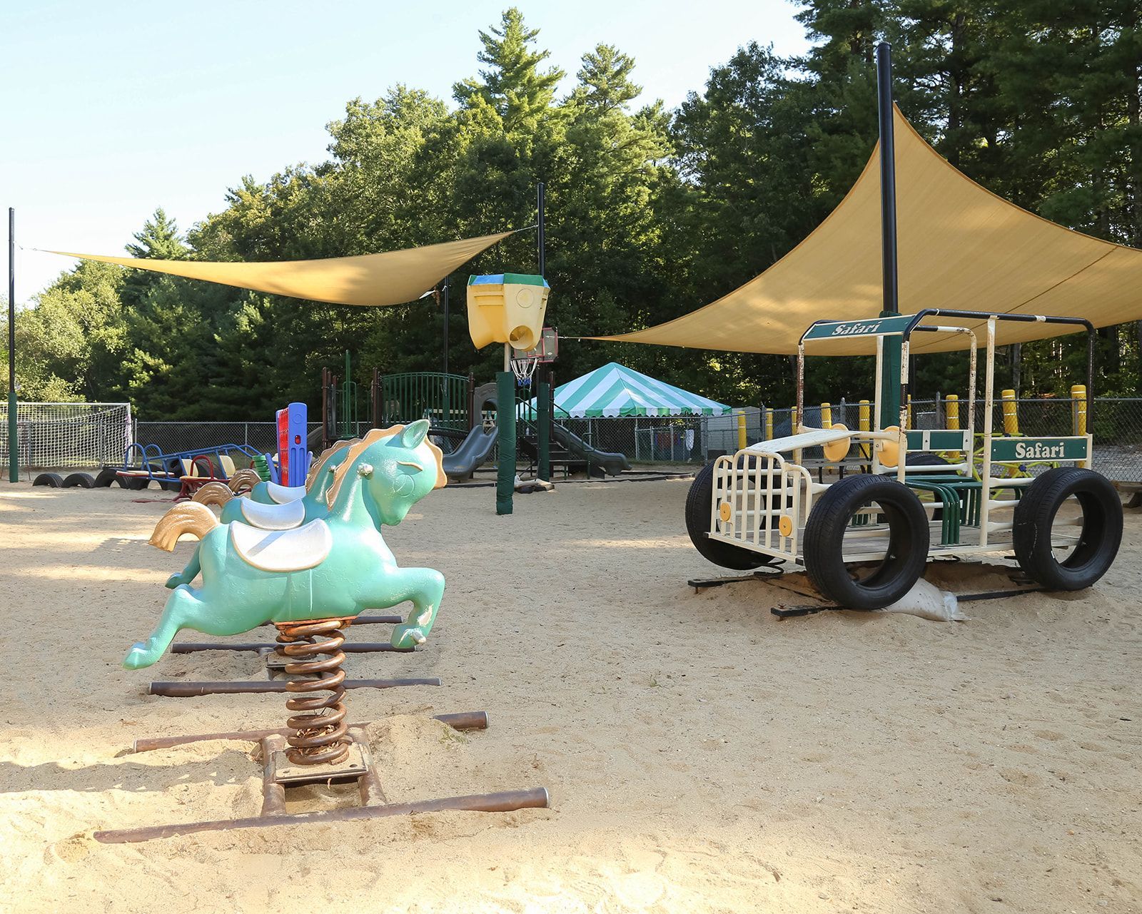 Playground with spring horse, construction vehicle, shade sails, and trees.