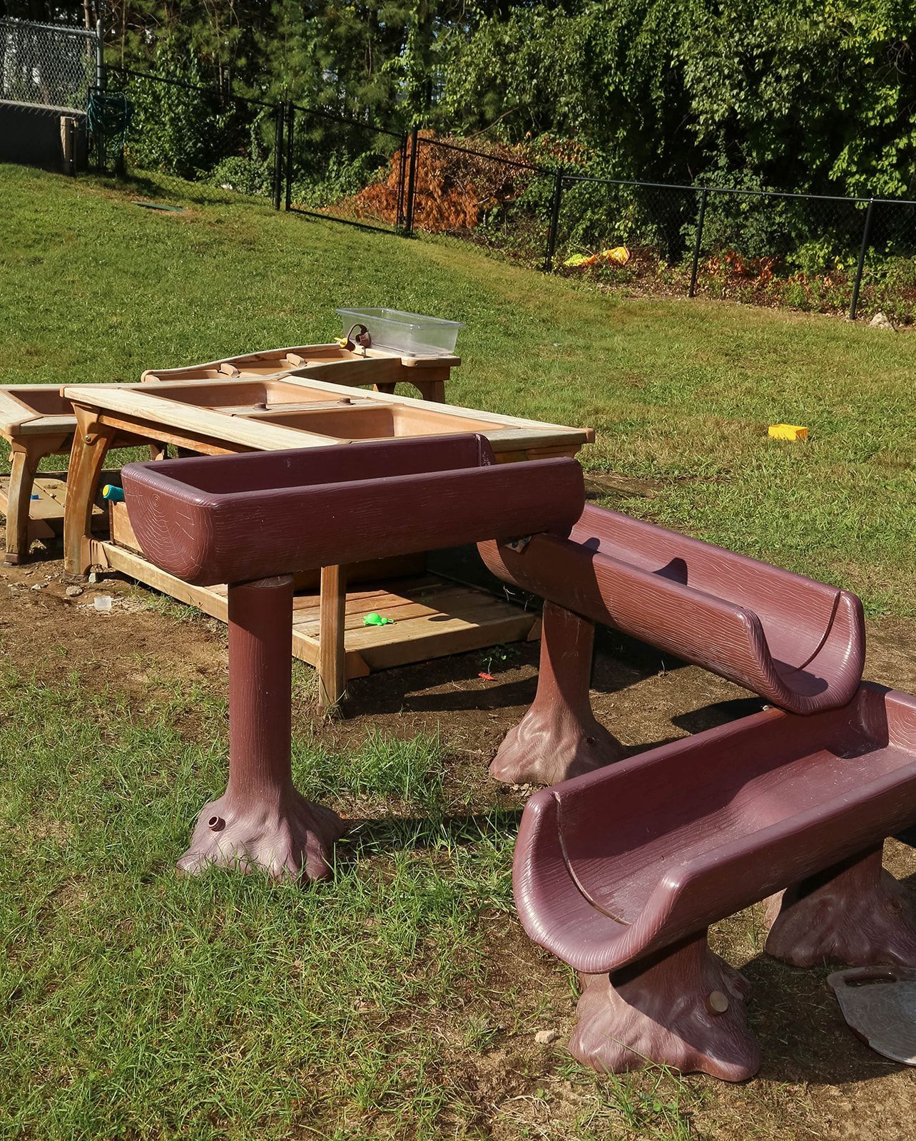 Outdoor play area with water tables and channels on grassy lawn.