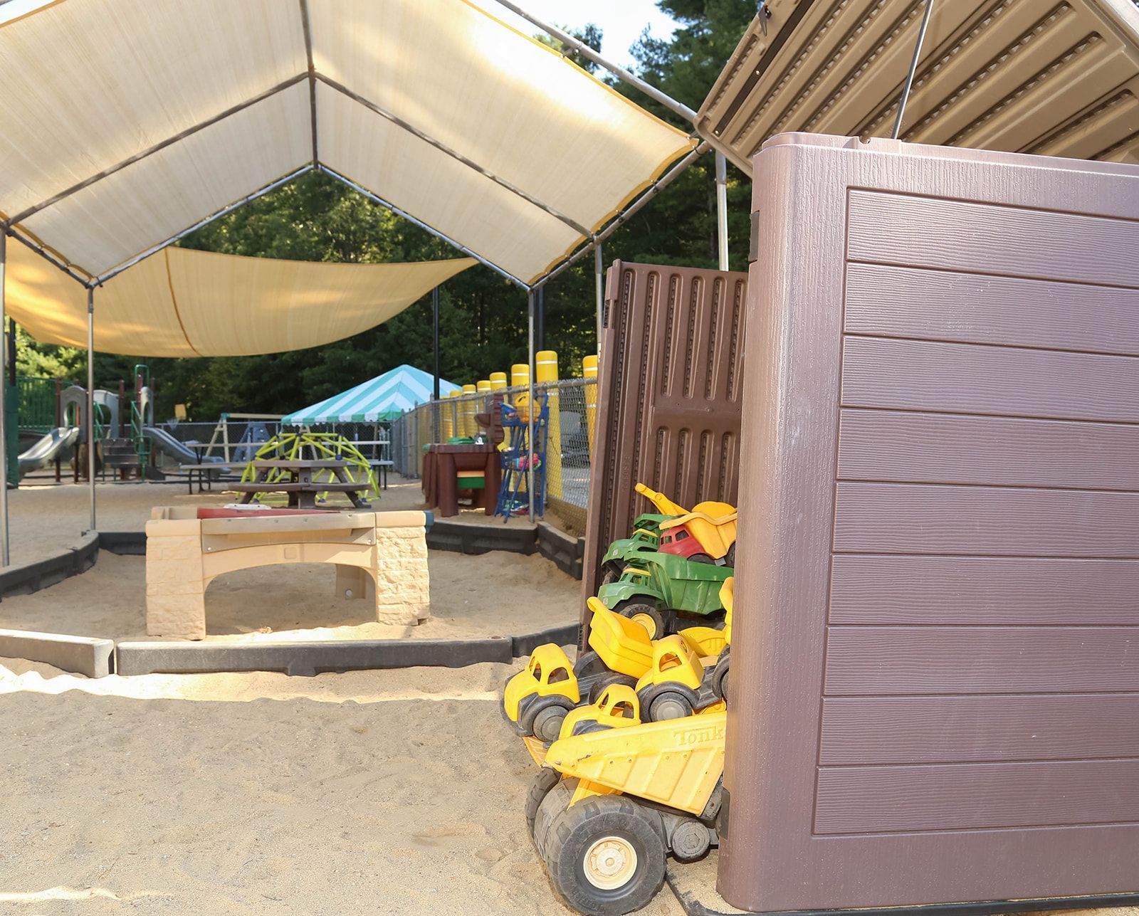 Playground sandbox with sunshades, toy trucks, and wooden walls.