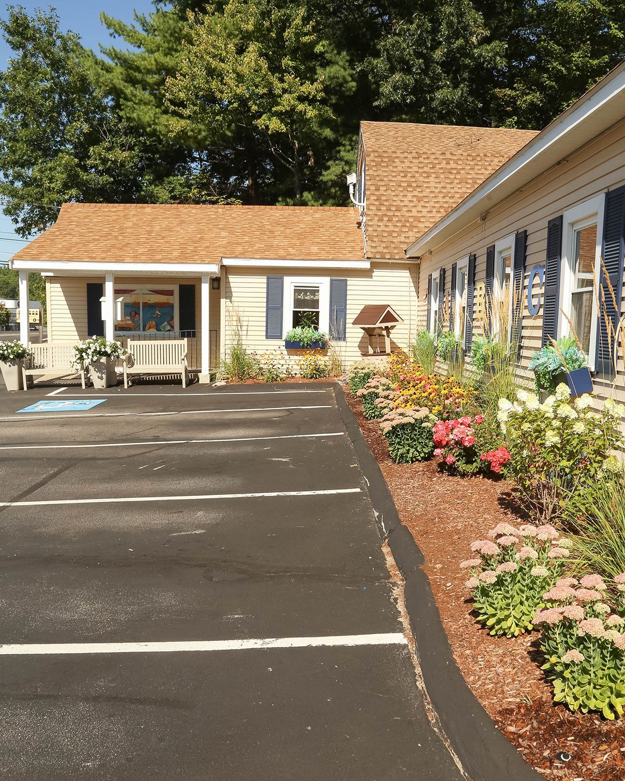 Entrance to a business with ramp, door, painted mural, and welcome mat. Cream-colored exterior with blue shutters.