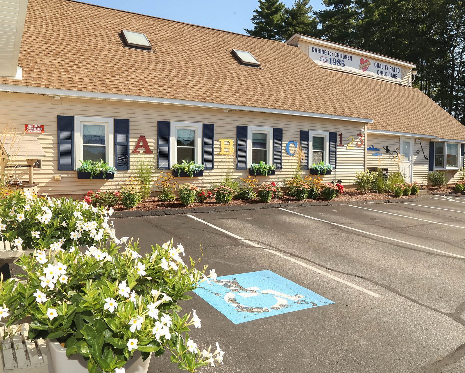 Exterior of a tan building with brown roof, blue shutters, flower boxes, and a handicap parking space.
