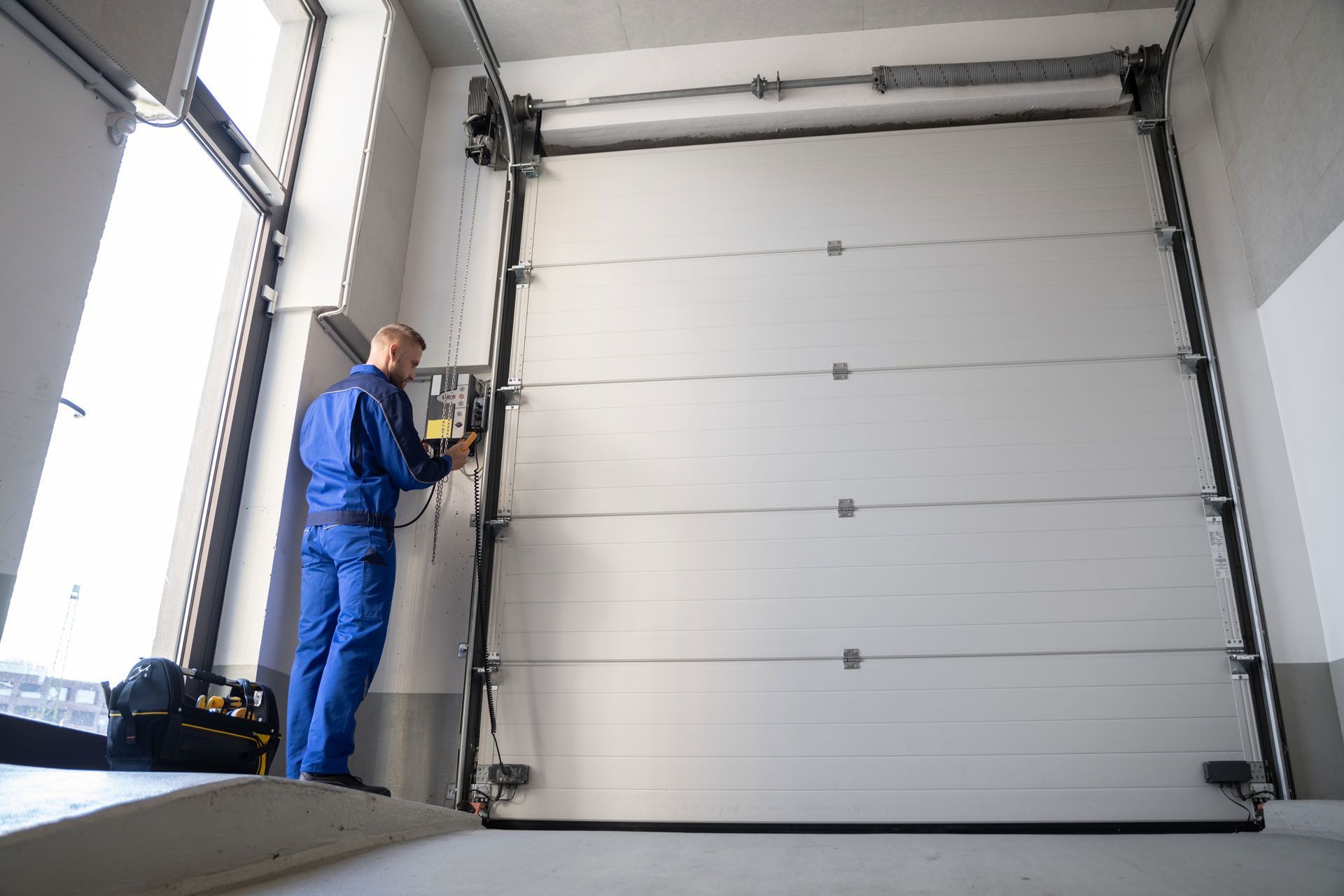 Man in blue overalls operating an industrial garage door inside a warehouse.