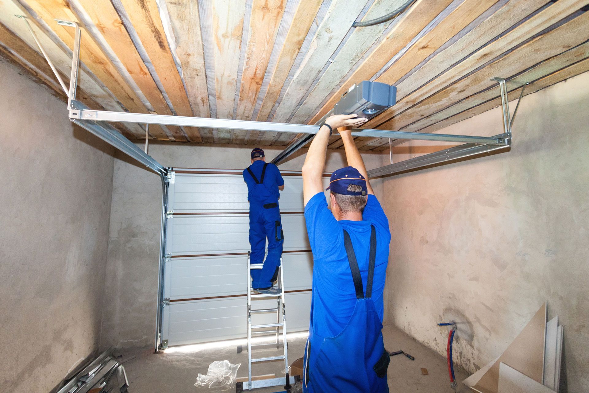 Two workers installing a garage door opener in a garage, one on a ladder.