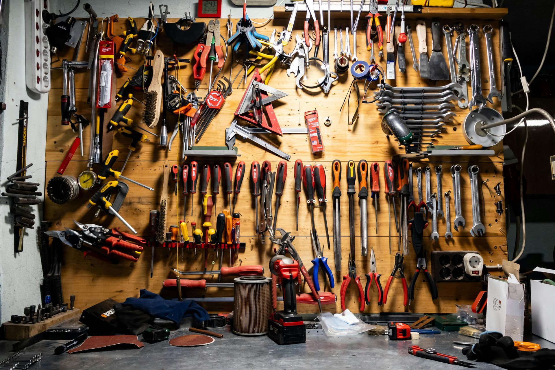 A wooden workshop wall densely packed with hung hand tools, including various wrenches, screwdrivers, and pliers.