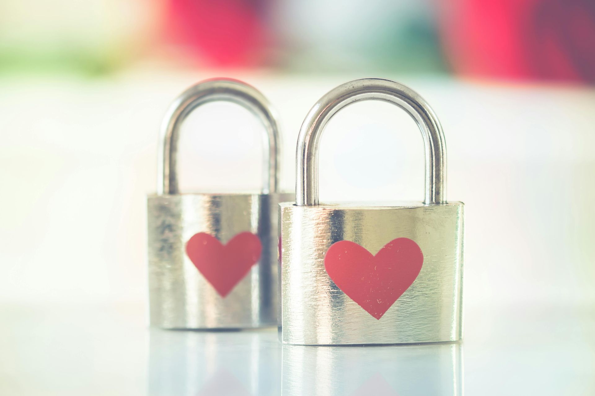 Two silver padlocks with red heart stickers, sitting side-by-side on a reflective surface.