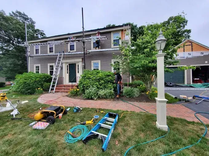 A man is standing in front of a house with a ladder in the grass.