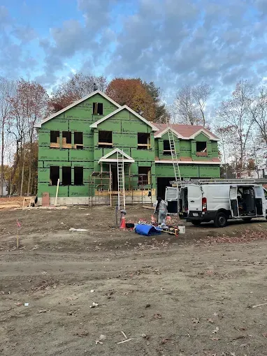 A house is being built in a dirt field with a van parked in front of it.