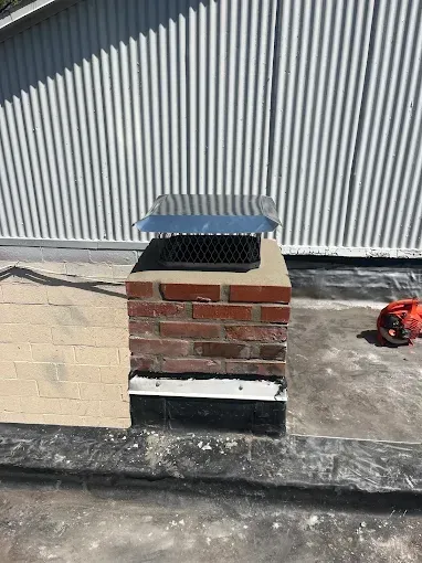 A brick chimney is sitting on top of a roof next to a building.