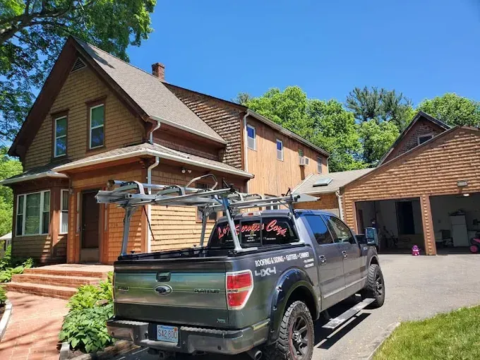 A truck with a ladder rack on the back is parked in front of a house.