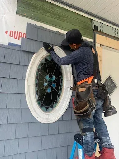 A man is standing on a ladder installing a round window.