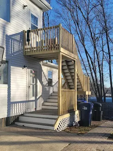 A white house with a wooden deck and stairs leading up to it.