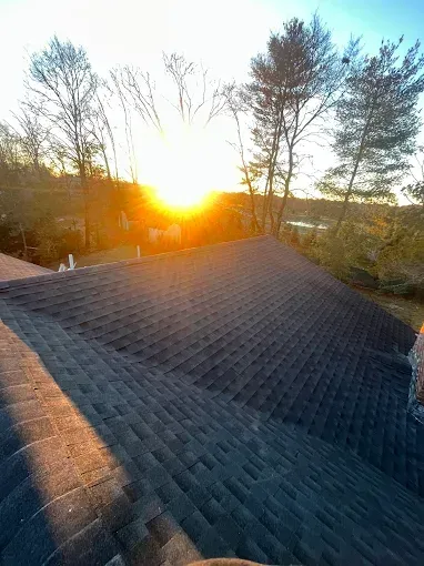 The sun is setting behind the trees on the roof of a house.