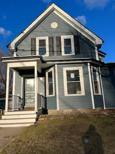 A large gray house with a porch and a blue sky in the background.